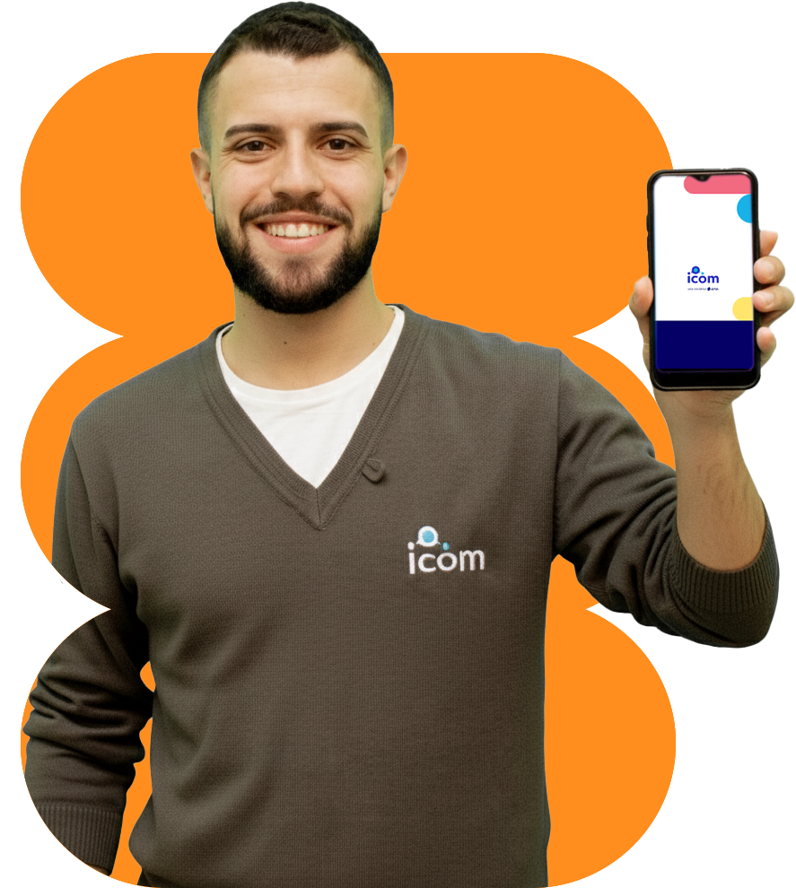 Homem sorridente com barba, vestindo um suéter cinza com o logo 'icom', segurando um smartphone que exibe o mesmo logo, posando em frente a um fundo laranja.